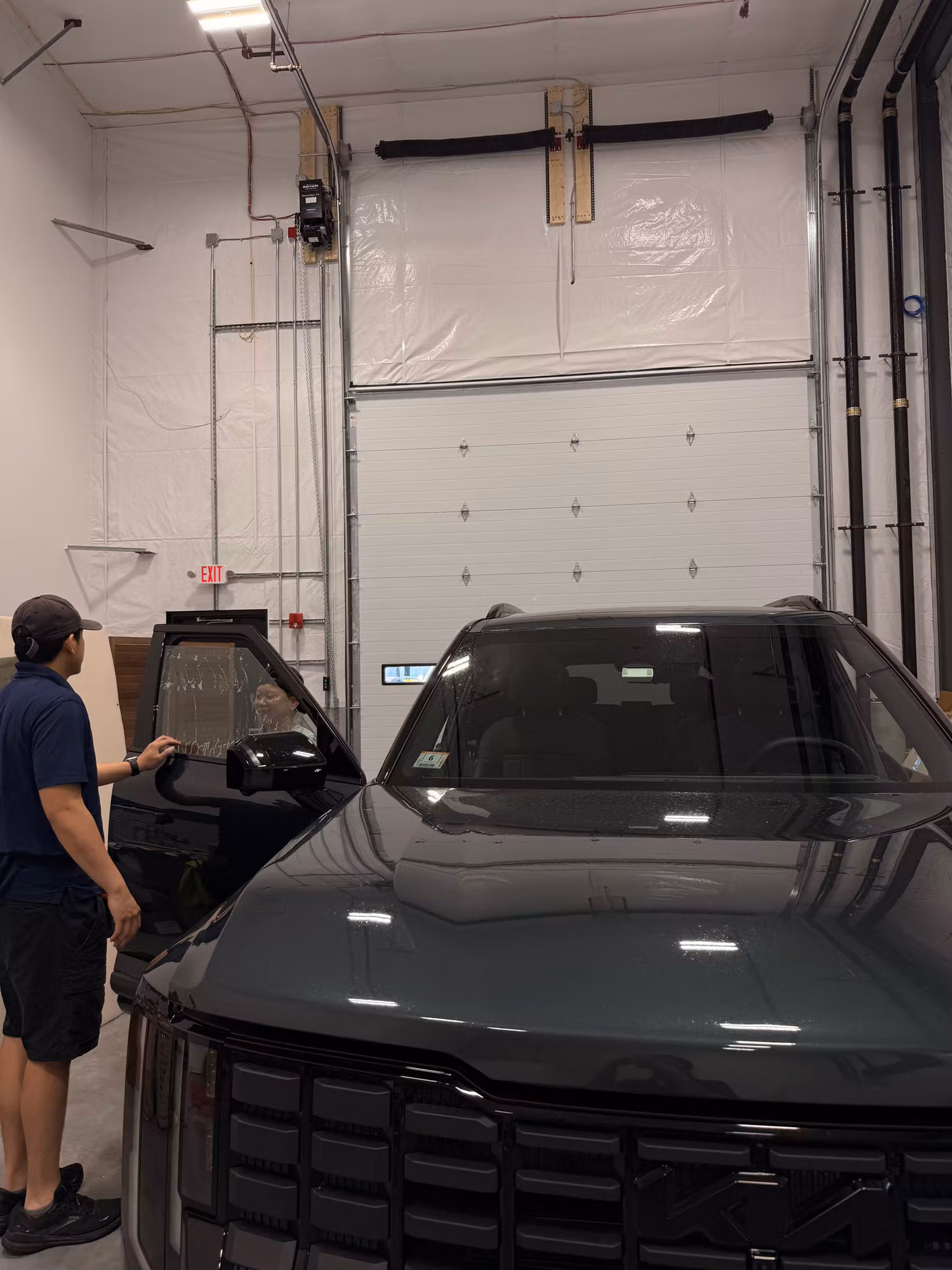 Installer prepping the front windshield and side glass of a dark SUV inside a window tint shop bay.