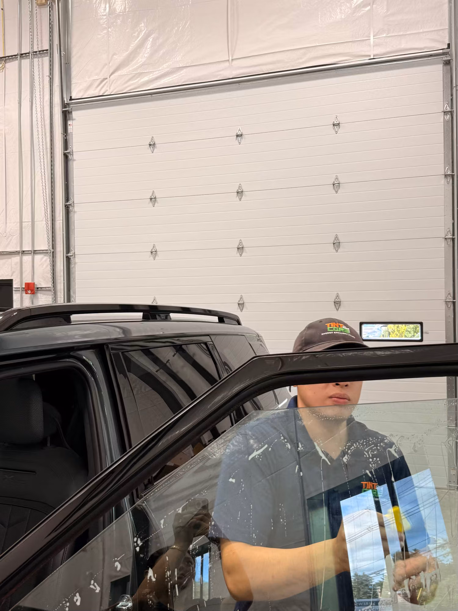 Installer working on the windshield of an SUV from inside the cabin during a tint application.
