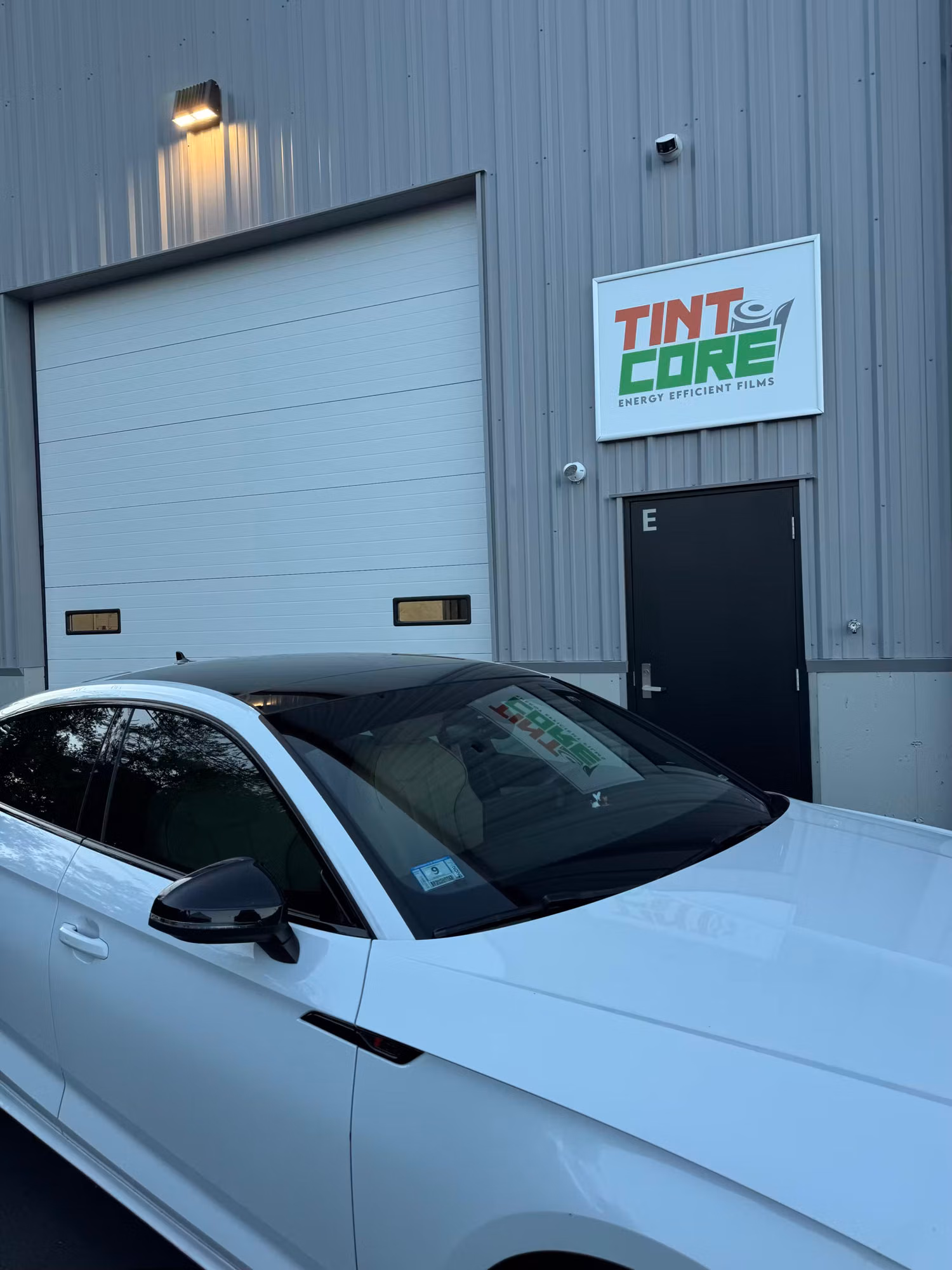 White sport sedan with freshly tinted front side window and dark glass parked outside the shop.