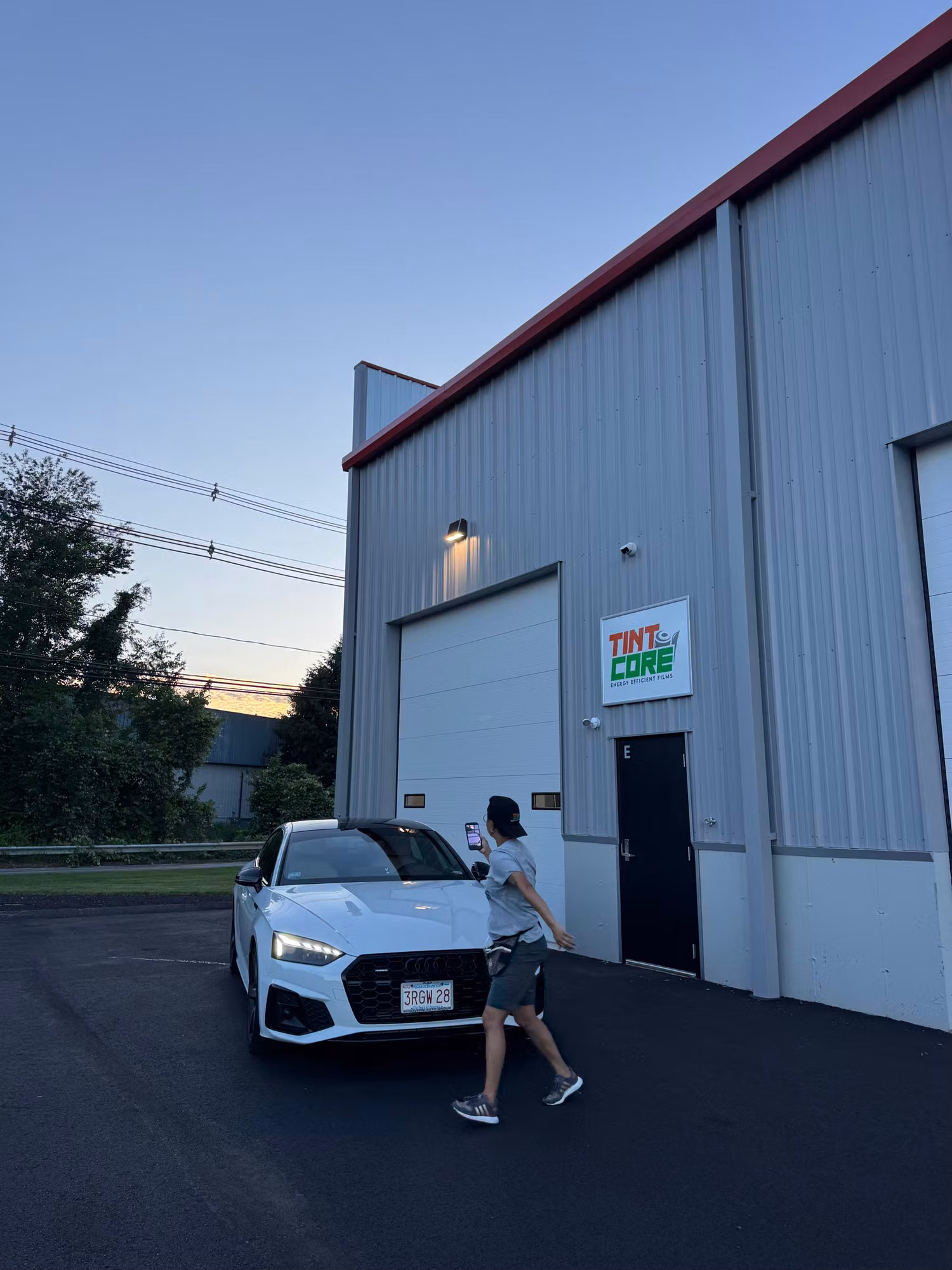 White sport sedan with tinted windows parked beside the shop at dusk after a tint installation.