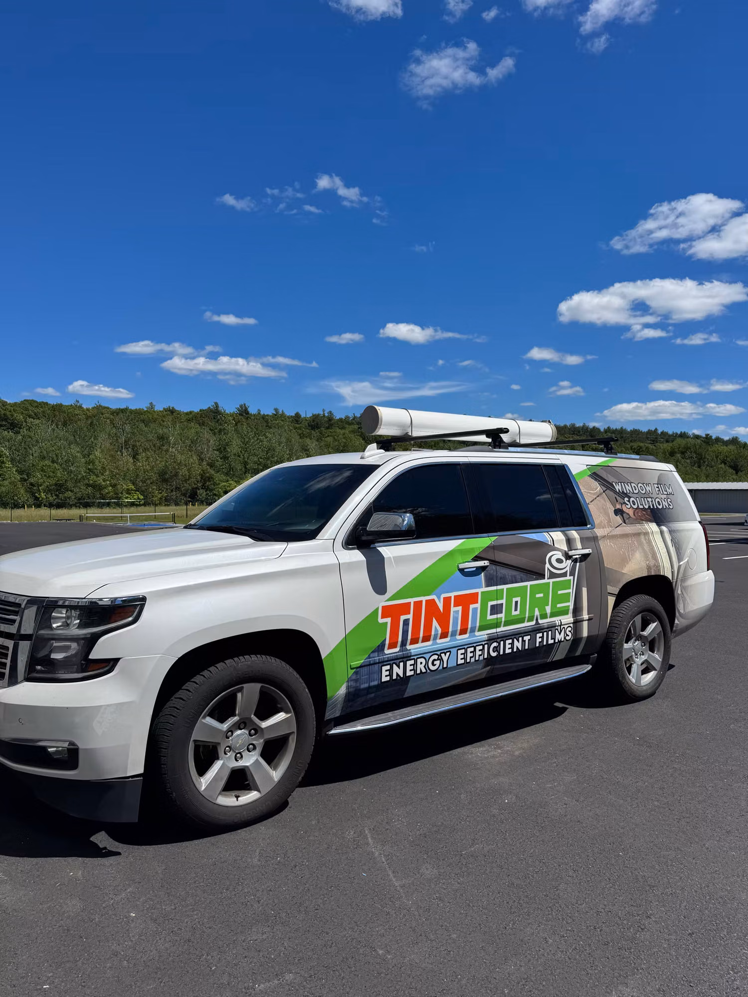 Branded service SUV with a roof-mounted film tube parked on open pavement under a blue sky with clouds.