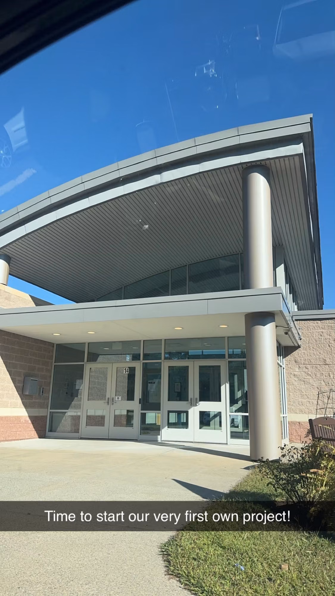 Exterior view of a building entrance with glass entry doors and a glazed vestibule beneath a curved canopy.