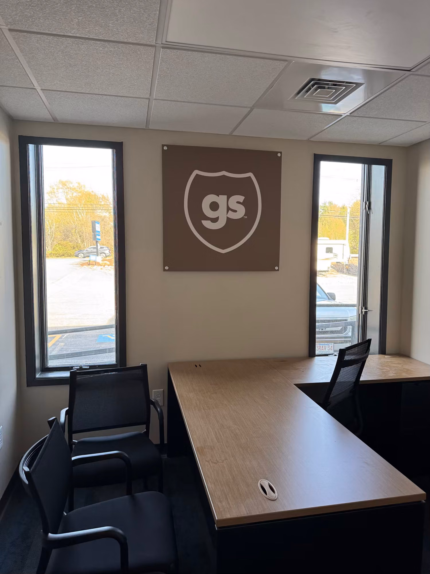 Small commercial office with two tall narrow windows flanking a wall sign above an L-shaped desk.