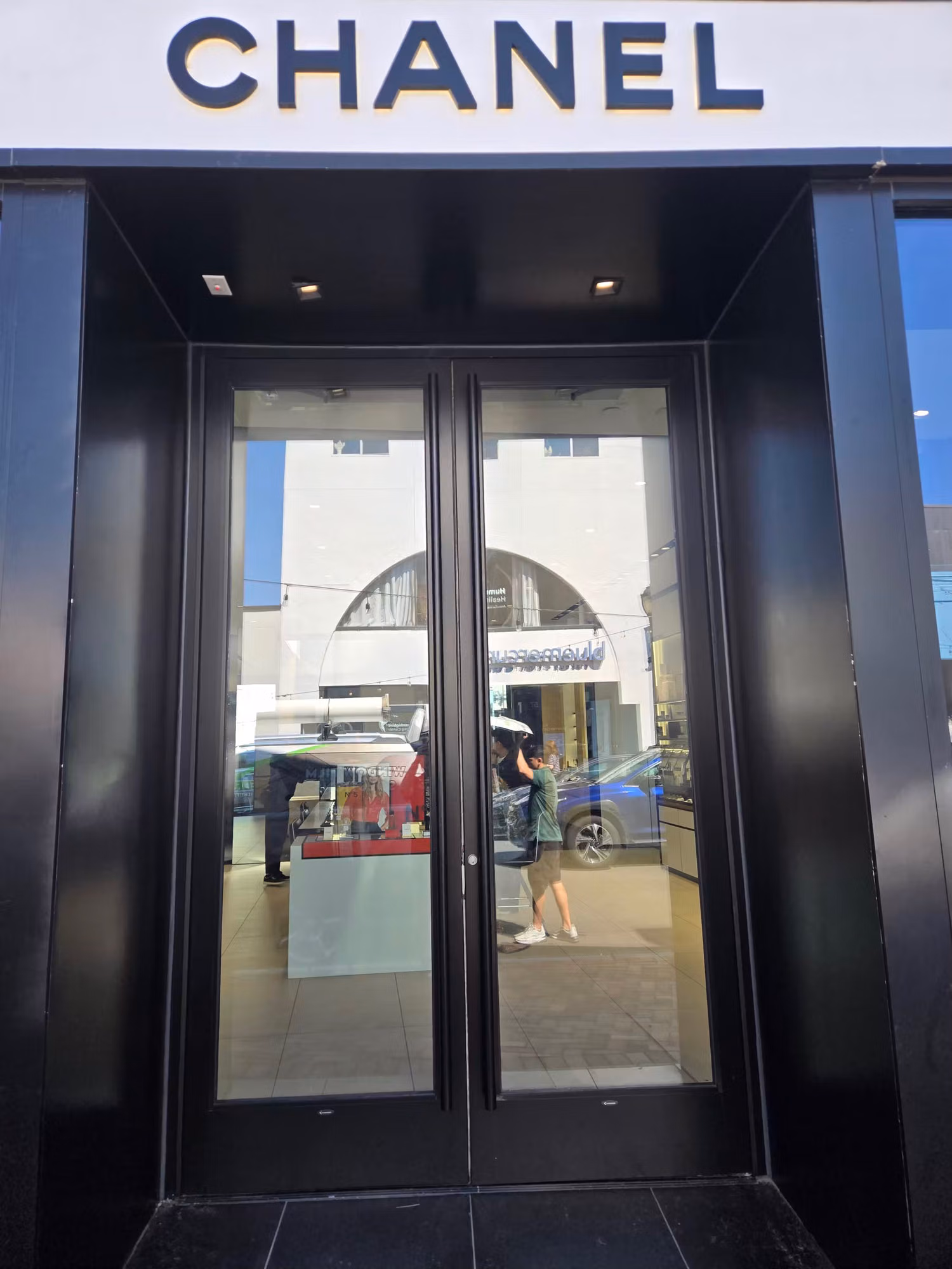 Black-framed glass double entry doors of a boutique storefront with clear protective film and interior visible through the glass.