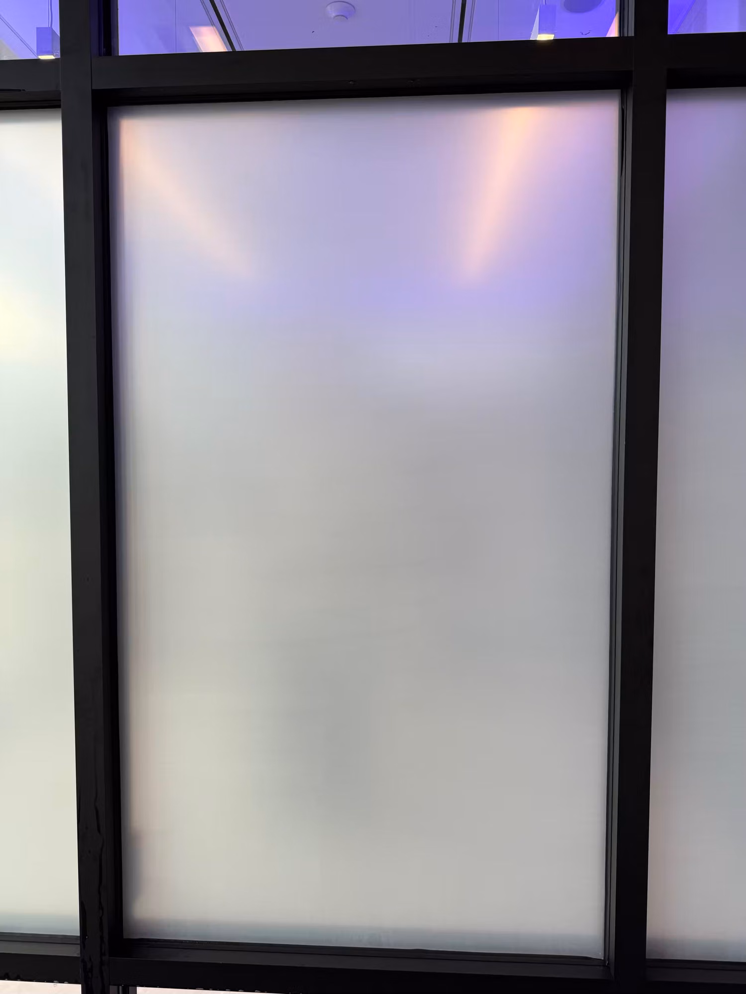 Frosted privacy film on an interior glass partition panel with clear transom glass visible above the black frame.