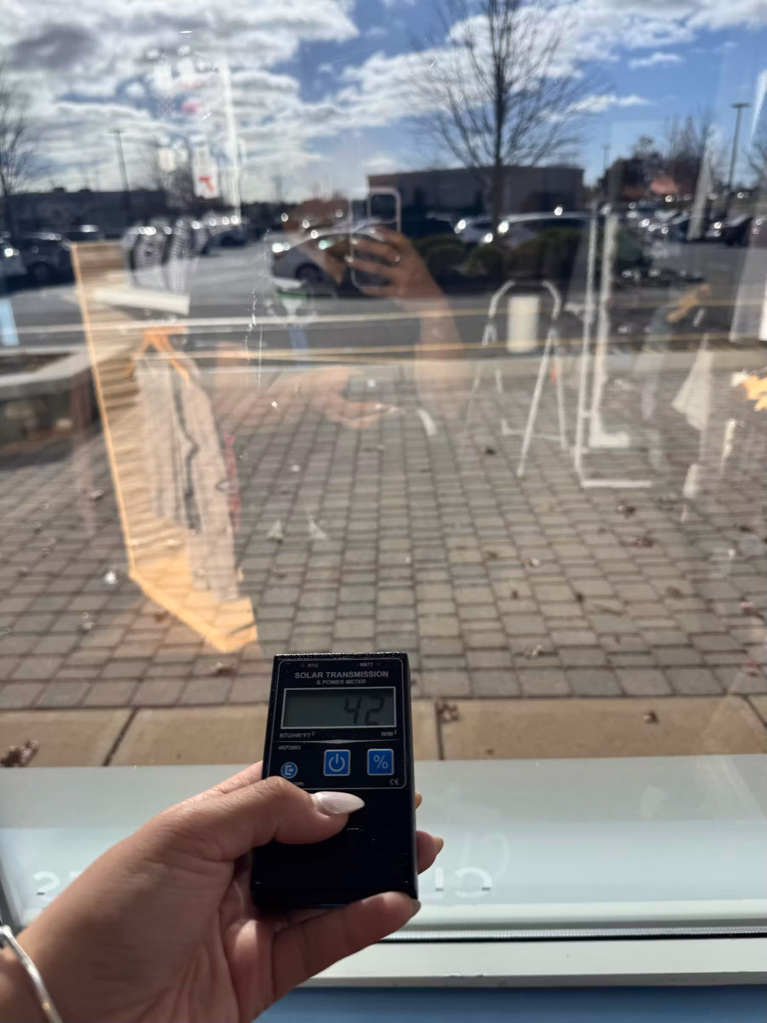 Hand holding a solar transmission meter reading 42 against a storefront window to verify film performance.