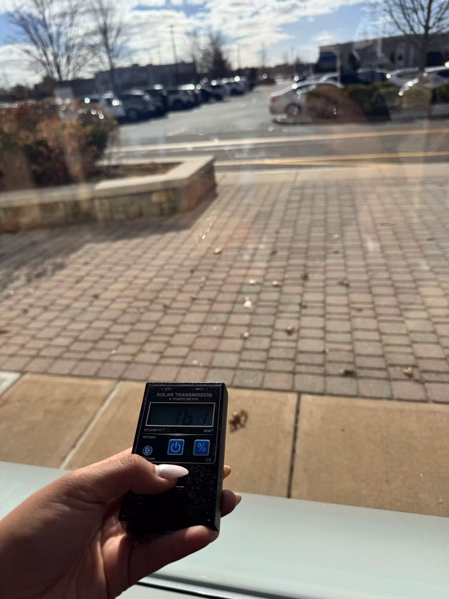 Hand holding a solar transmission meter against the lower storefront glass to measure light passing through the film.
