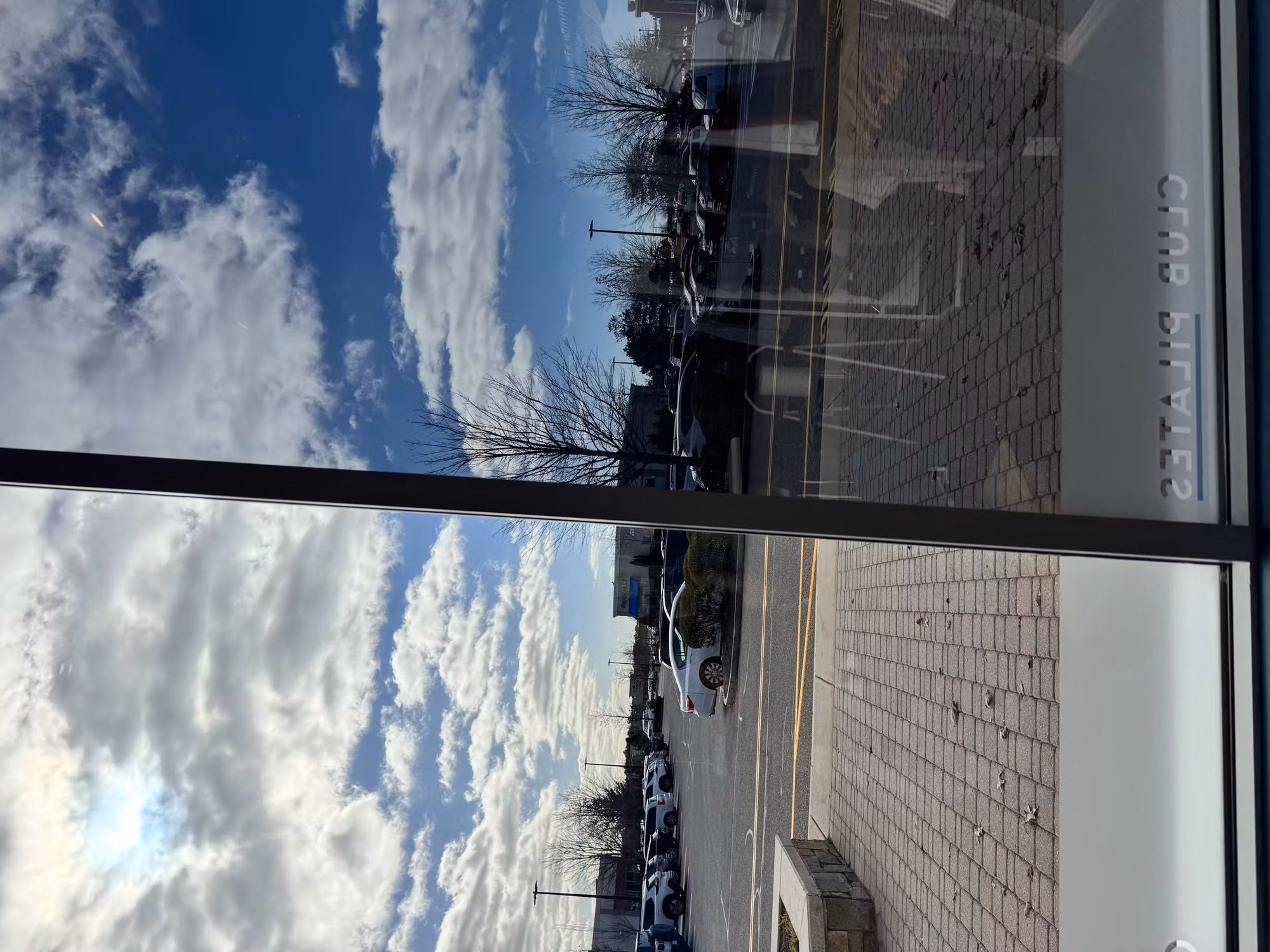 Interior view through a tinted storefront window looking out toward a sunlit parking lot.