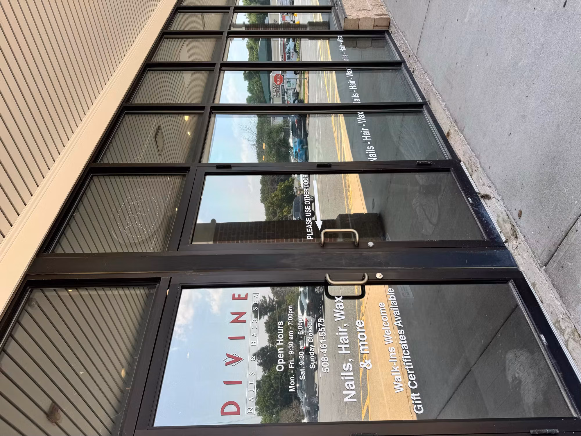 Salon glass entry door and adjacent window wall with cut vinyl logo, hours, and service lettering on the glass.