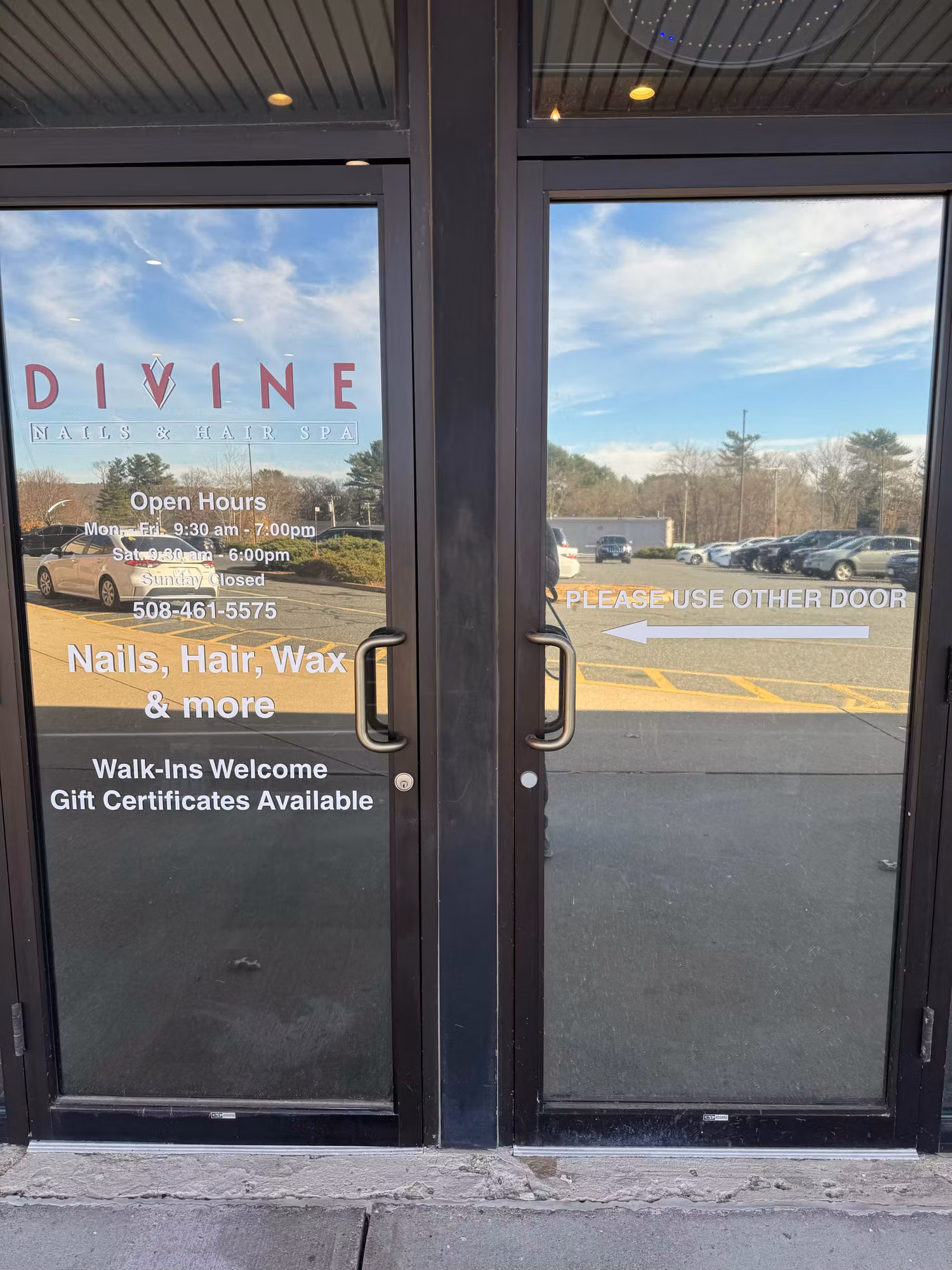 Double glass entry doors with cut vinyl salon logo, business hours, and service lettering applied to the glass.