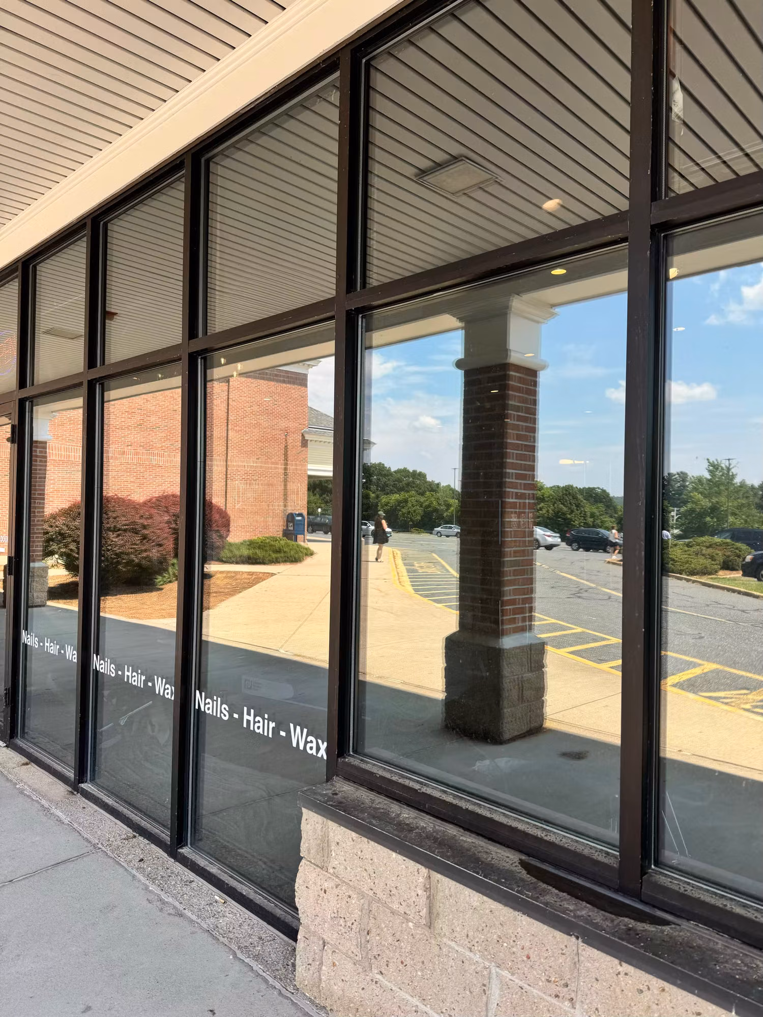 Salon storefront window wall with cut vinyl service lettering applied across the glass next to a brick column.