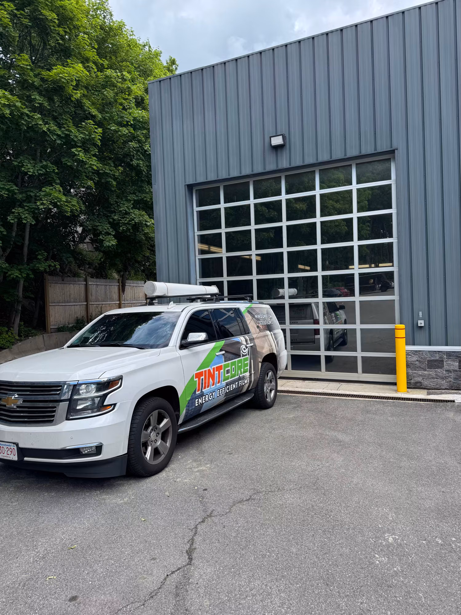 Service vehicle parked beside a gray metal commercial building with a large multi-pane glass overhead door.