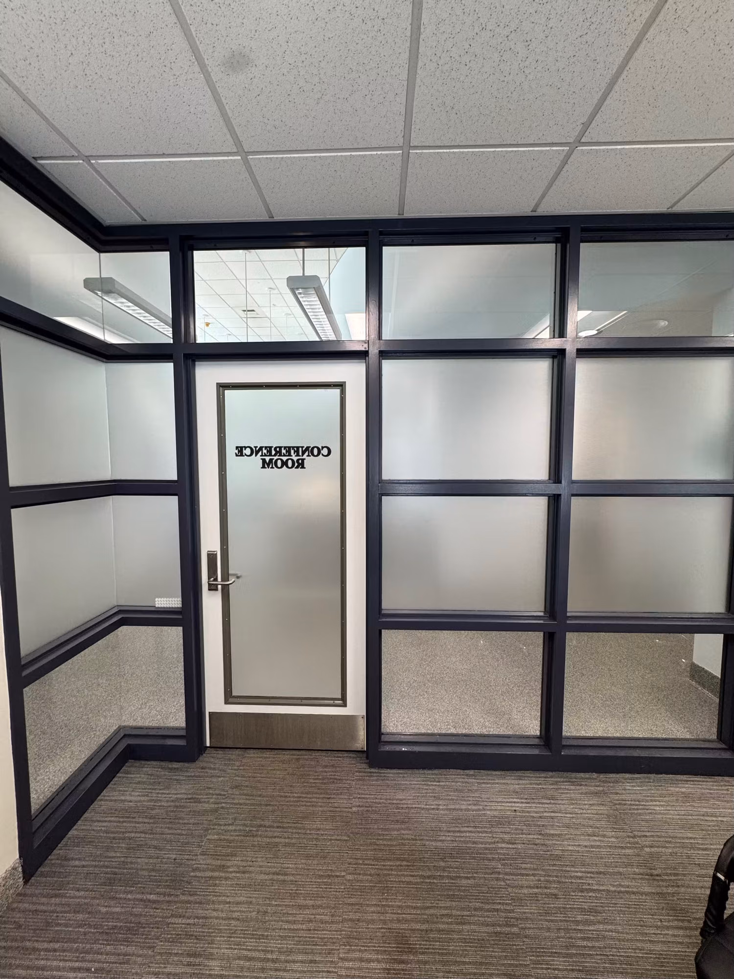 Office conference room enclosed by black-framed glass partitions with a frosted privacy band and a frosted Conference Room door.