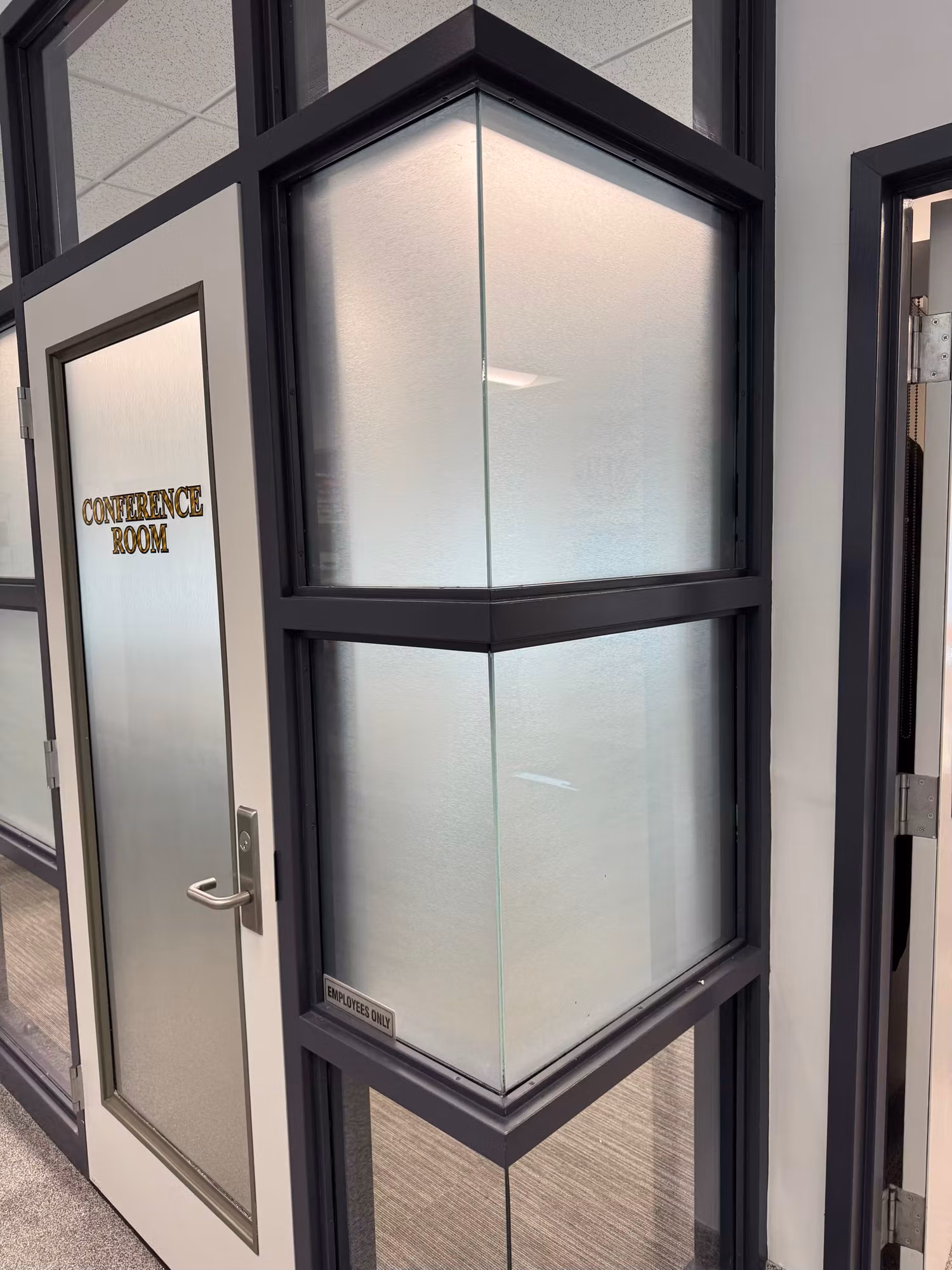 Corner of an office conference room with frosted privacy film on the glass partition and a frosted Conference Room door.