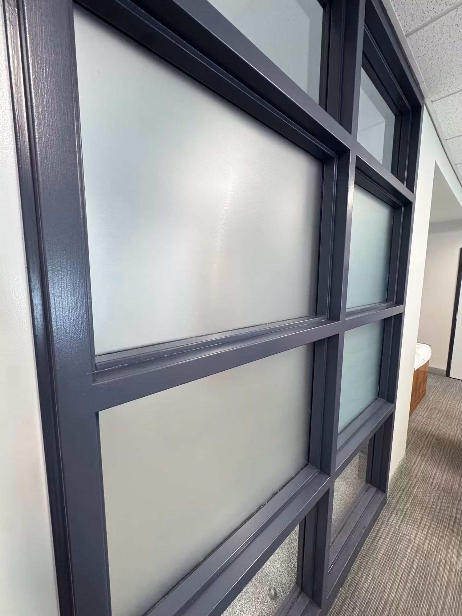Close-up of a dark-framed interior glass partition wall with frosted privacy film applied to the panes.