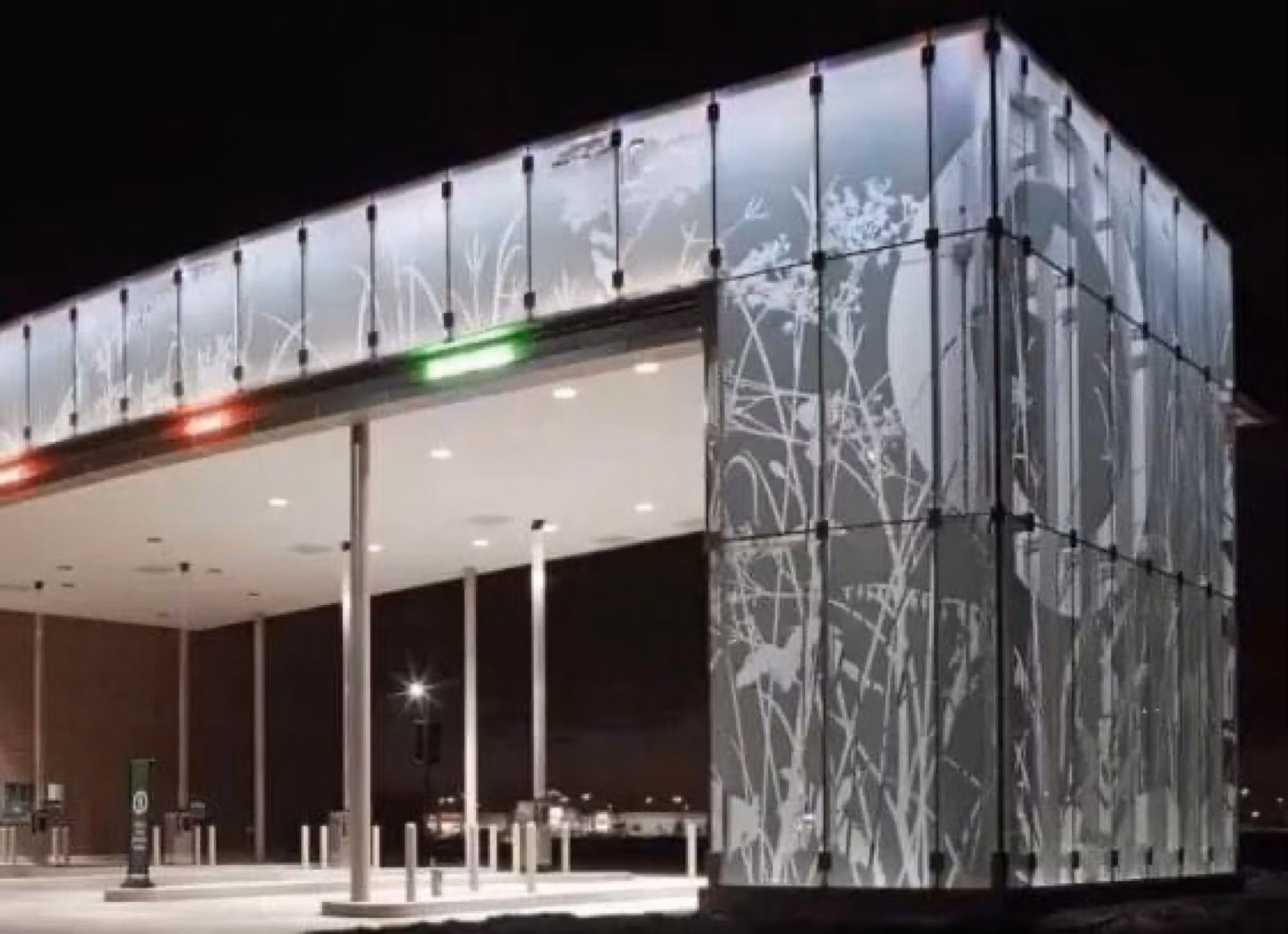 Illuminated glass building facade featuring an etched botanical grass pattern across the panels at night.