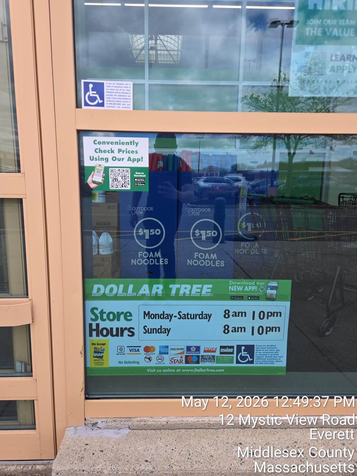 Retail storefront window with printed promotional posters and store-hours decals applied to the glass.