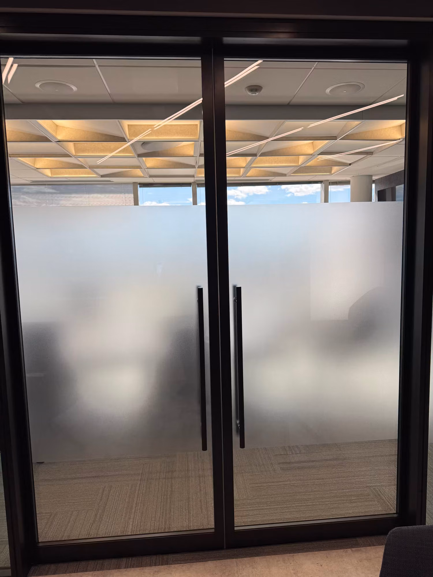 Double glass entry doors covered with frosted privacy film leaving clear glass at the top transom.