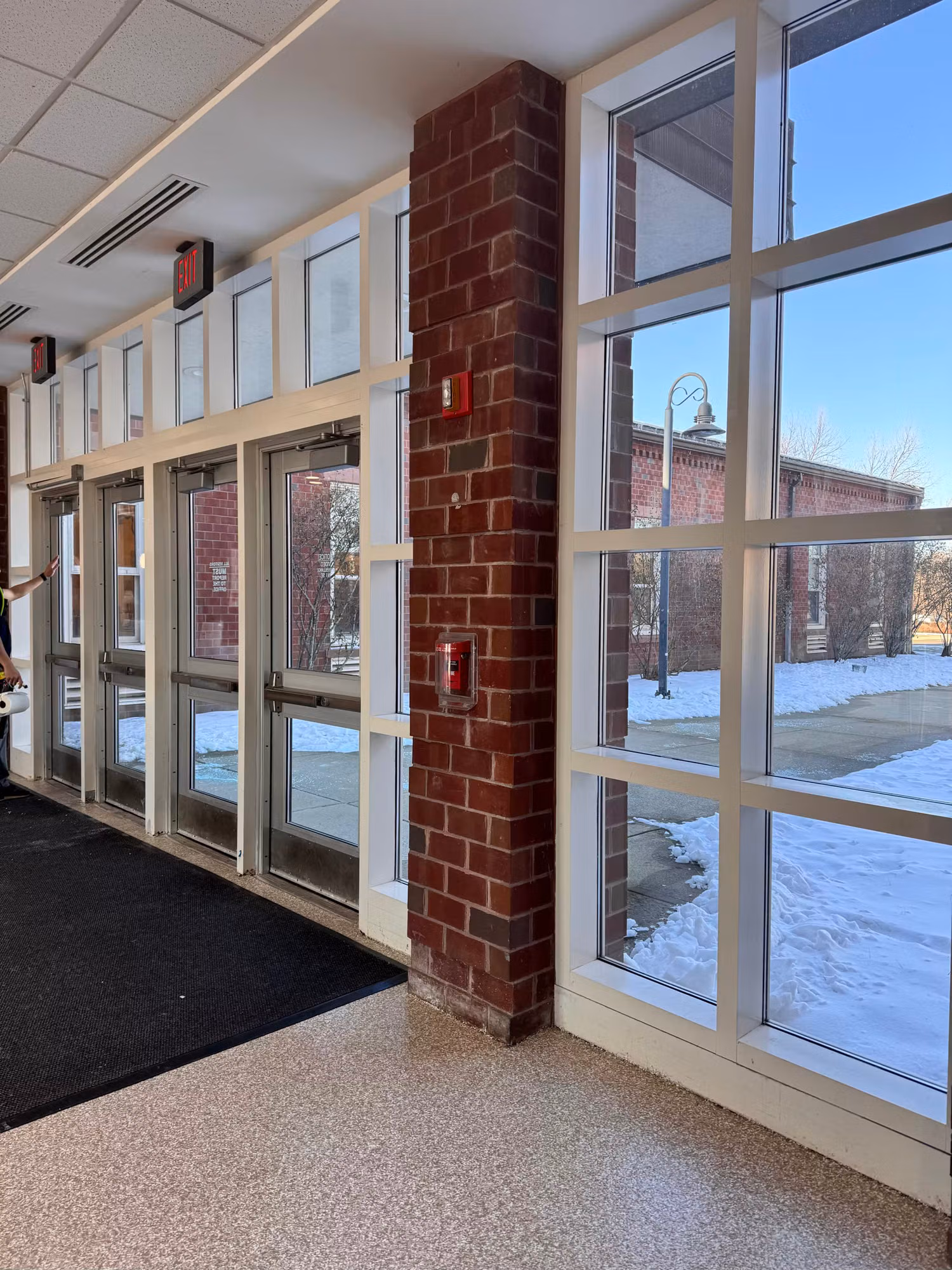 Entrance hallway with glass doors and a tall mullioned window wall beside a brick column with snow outside.