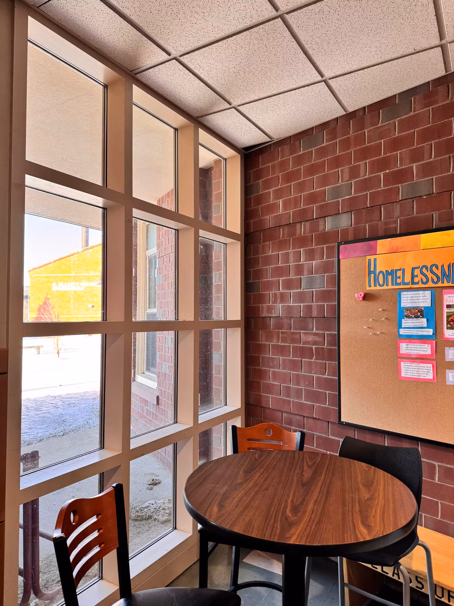 Interior seating nook with a clear-glass mullioned window wall beside a brick wall in a commercial building.