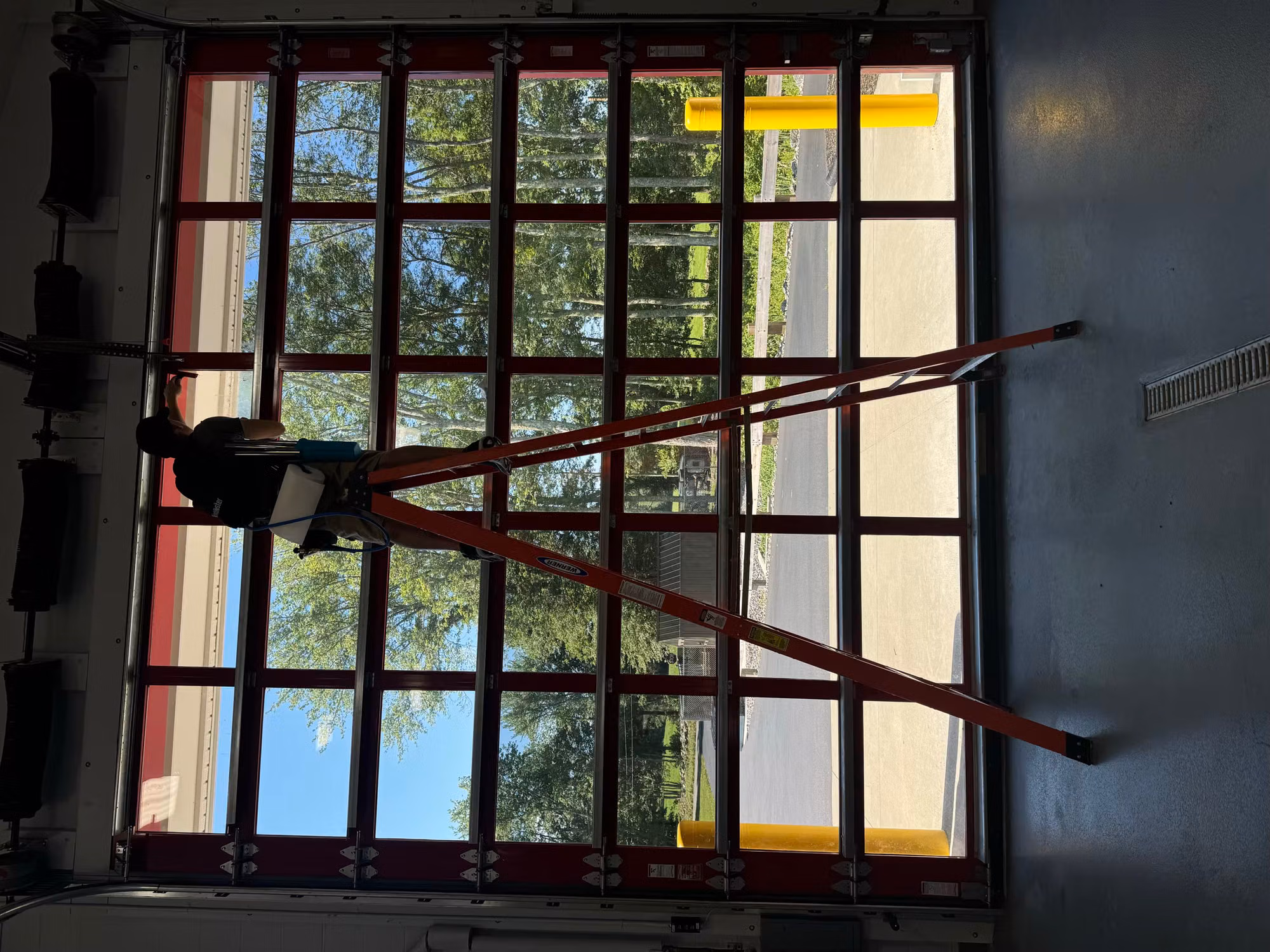 Installer on a ladder applying window film to the glass panels of a fire station bay door.