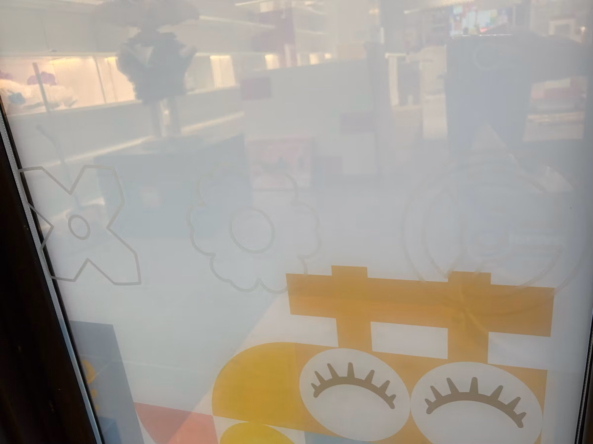 Close-up of storefront glass with frosted decorative film showing gear and floral patterns over colorful printed graphics.