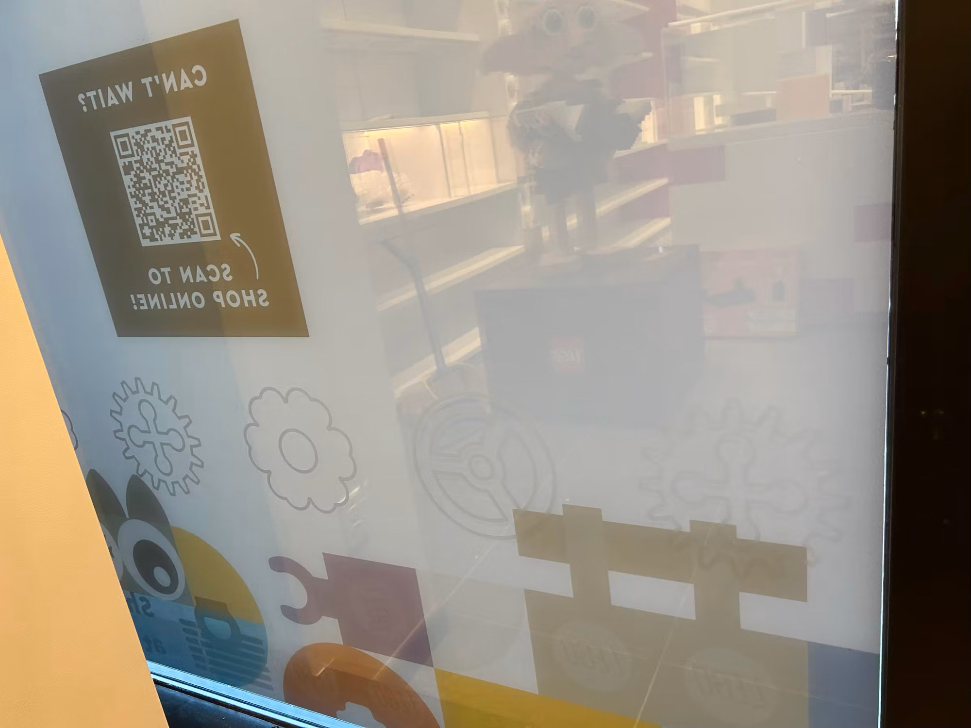 Storefront window with frosted decorative film featuring gear and puzzle motifs alongside a scan-to-shop QR graphic panel.