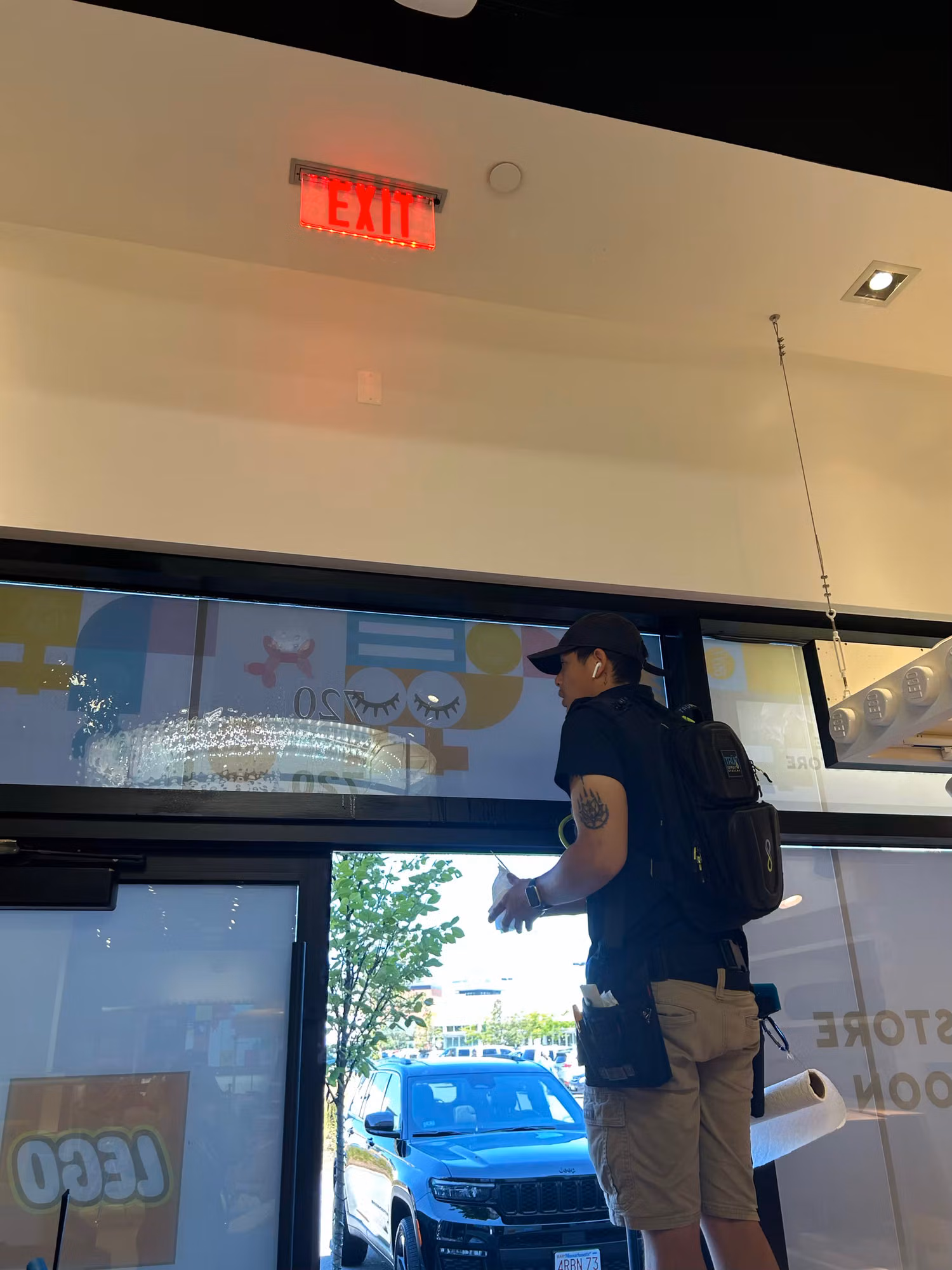 Interior view through retail storefront glass doors covered with colorful printed window graphics as a worker stands at the entry.