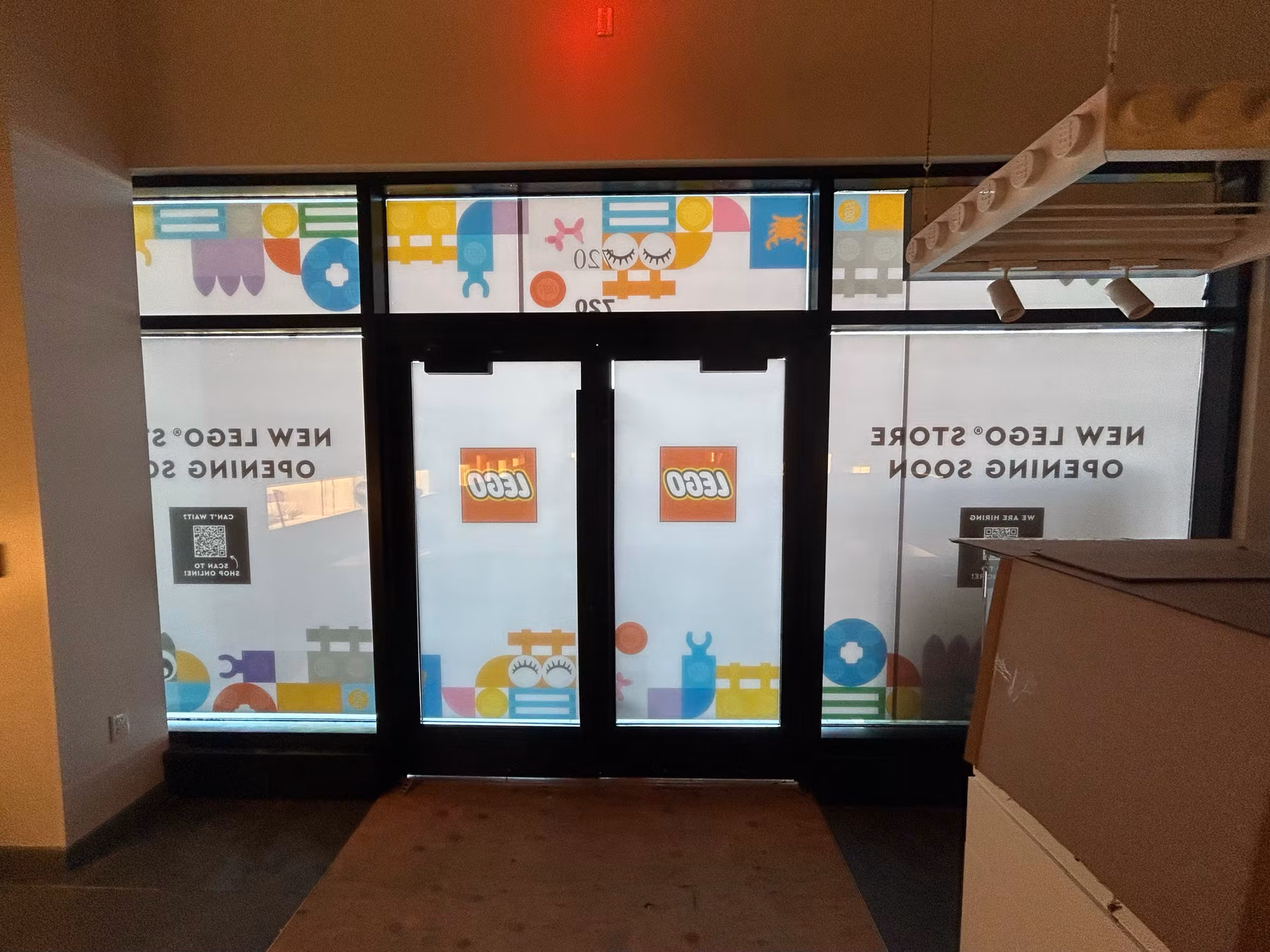 Retail storefront entry doors and sidelights wrapped in colorful printed window graphics announcing a new store opening soon.