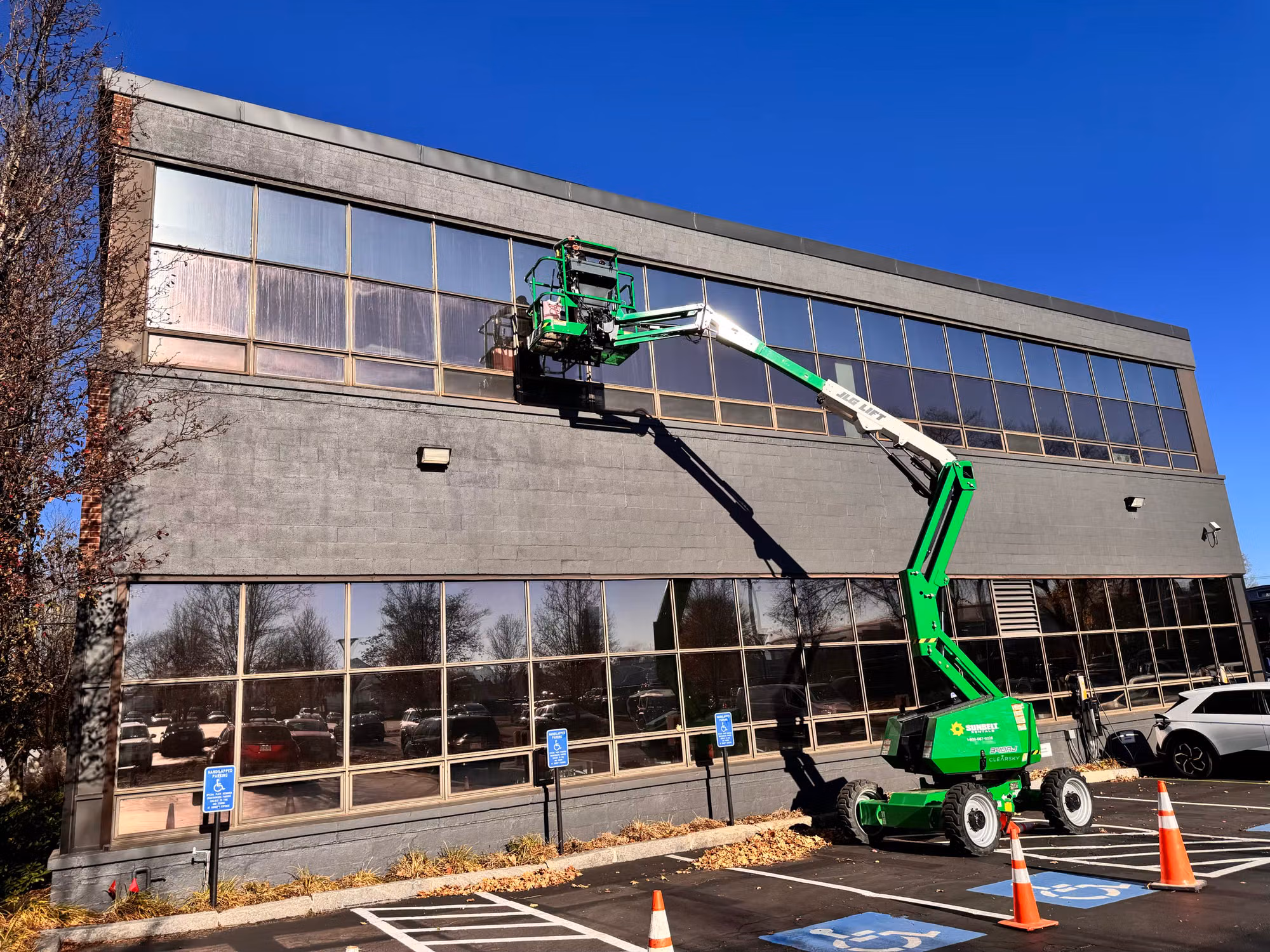 Side view of a boom lift extended to the second-floor windows of an office building during window film installation.