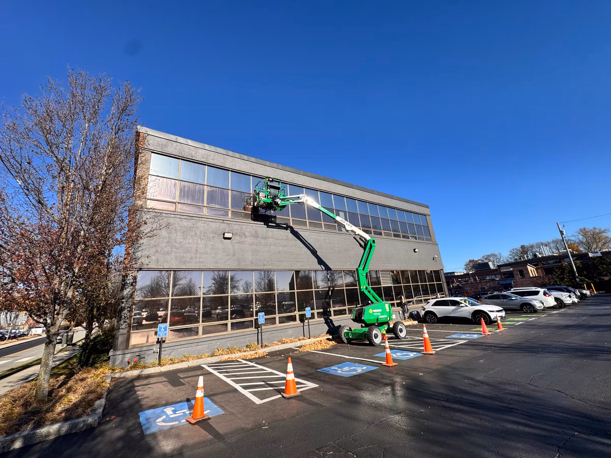 Boom lift reaching the upper windows of a gray office building as window film is applied to the glass.