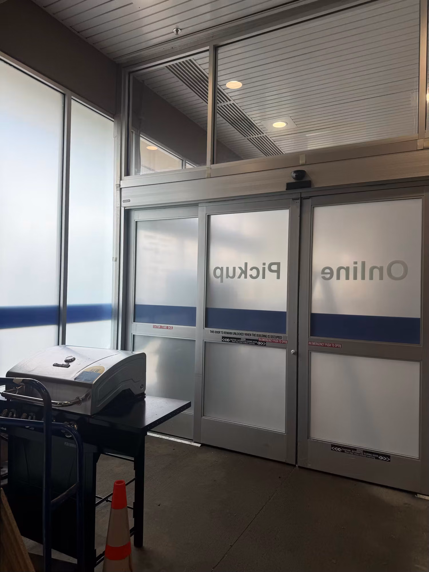 Interior view of automatic sliding entry doors showing applied Online Pickup vinyl graphics with frosted band and blue stripe.