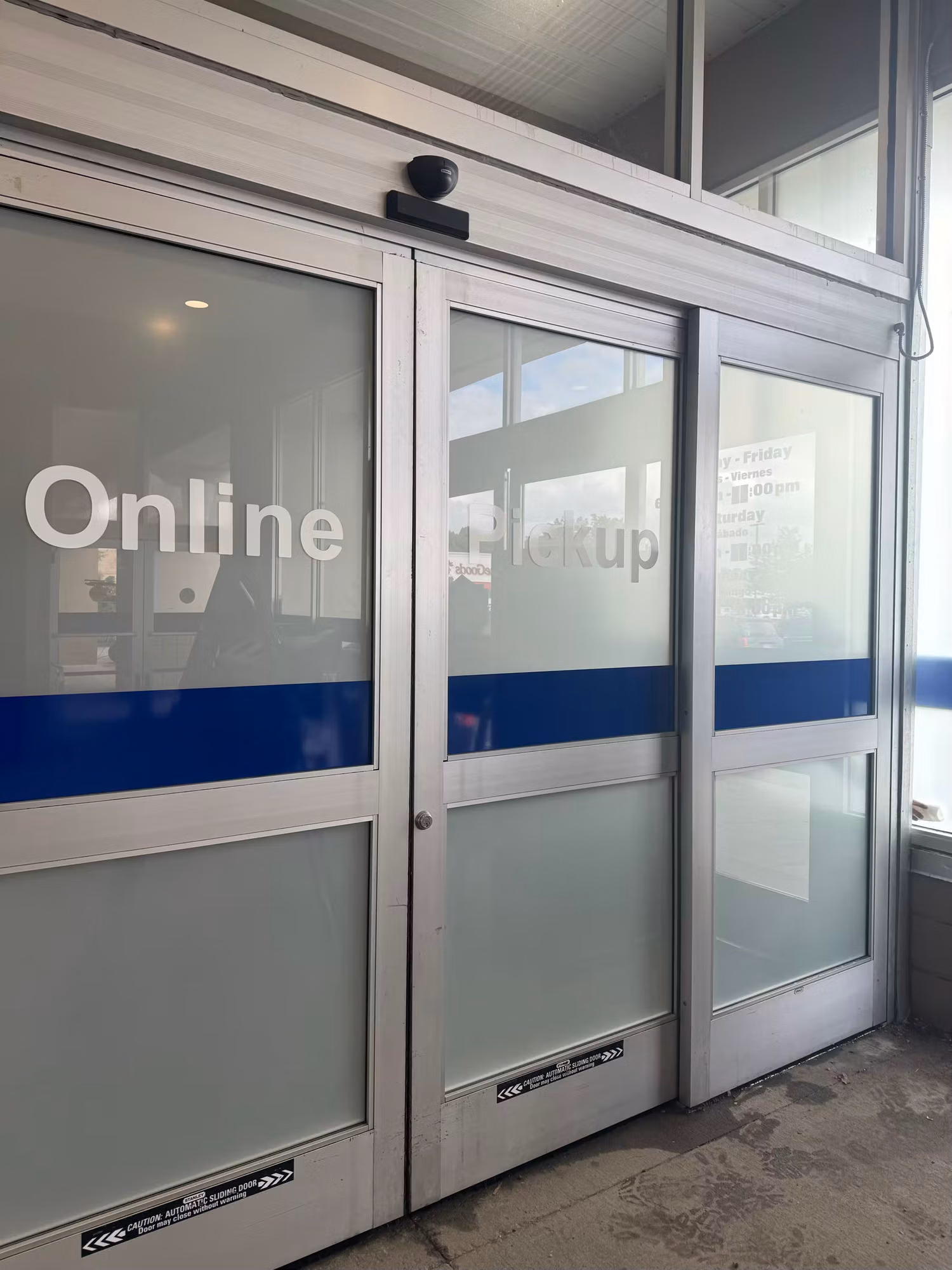 Close exterior view of sliding storefront doors with Online Pickup cut-vinyl lettering, a blue stripe, and frosted lower glass.