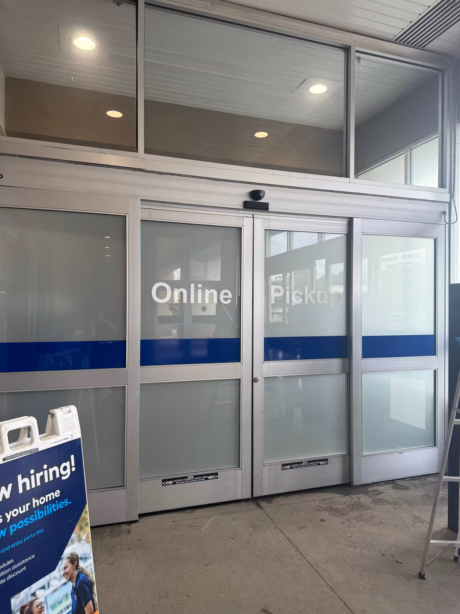 Exterior of sliding entry doors with Online Pickup vinyl lettering and transom windows above during an installation.