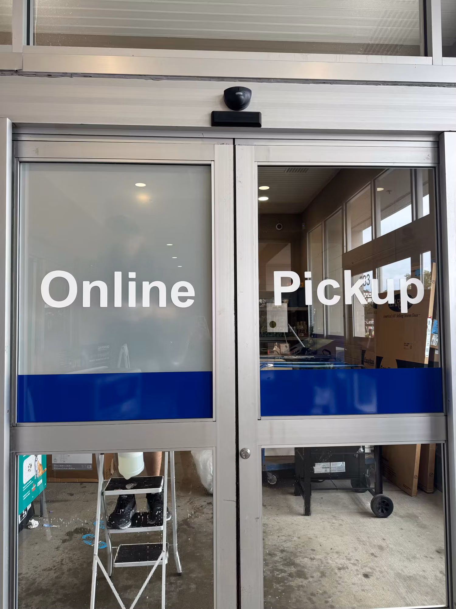 Close exterior view of glass entry doors with bold Online Pickup cut-vinyl lettering and a blue graphic stripe.