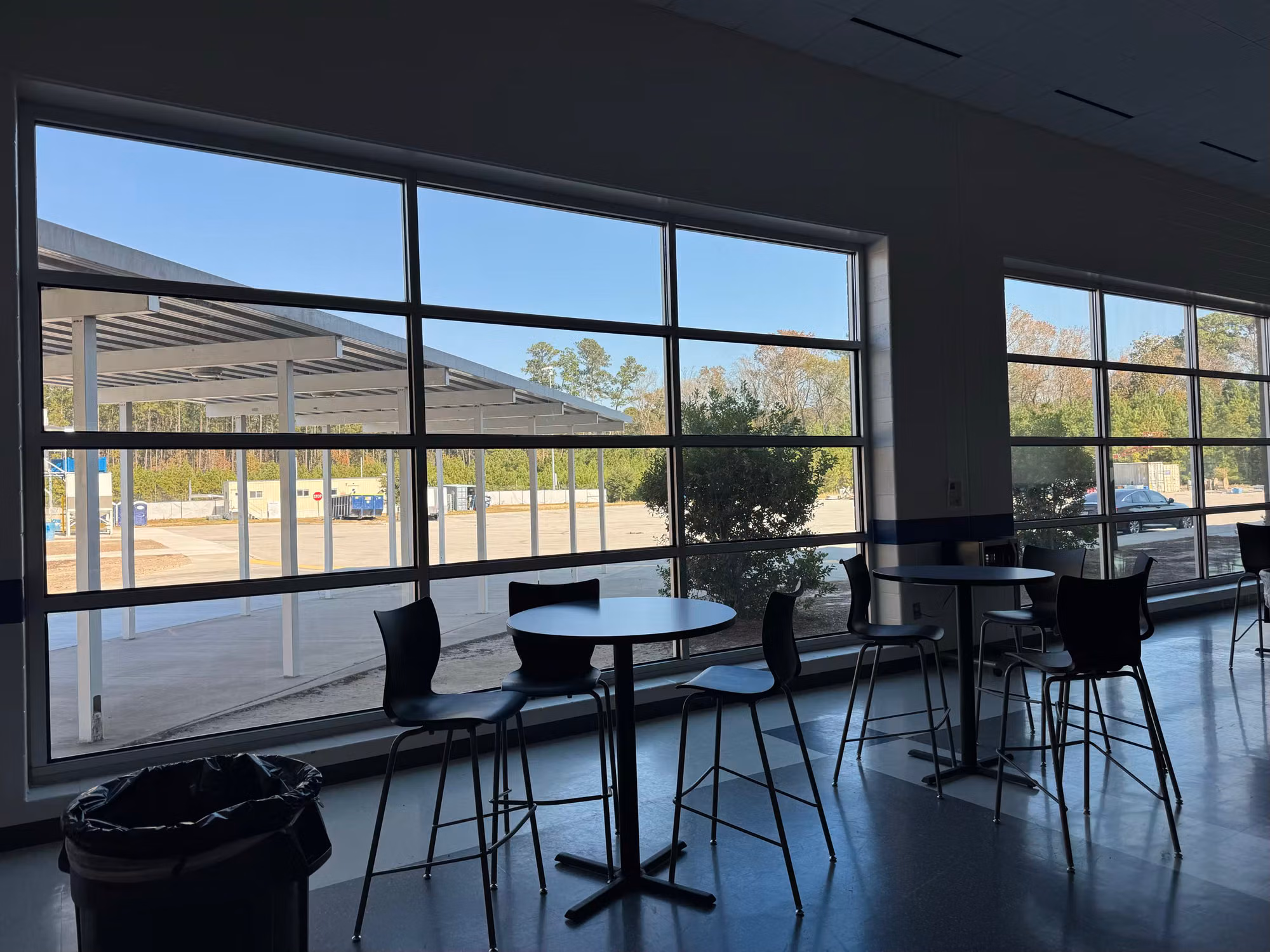 Floor-to-ceiling cafeteria window wall with tinted glass and bar-height seating facing a parking lot.