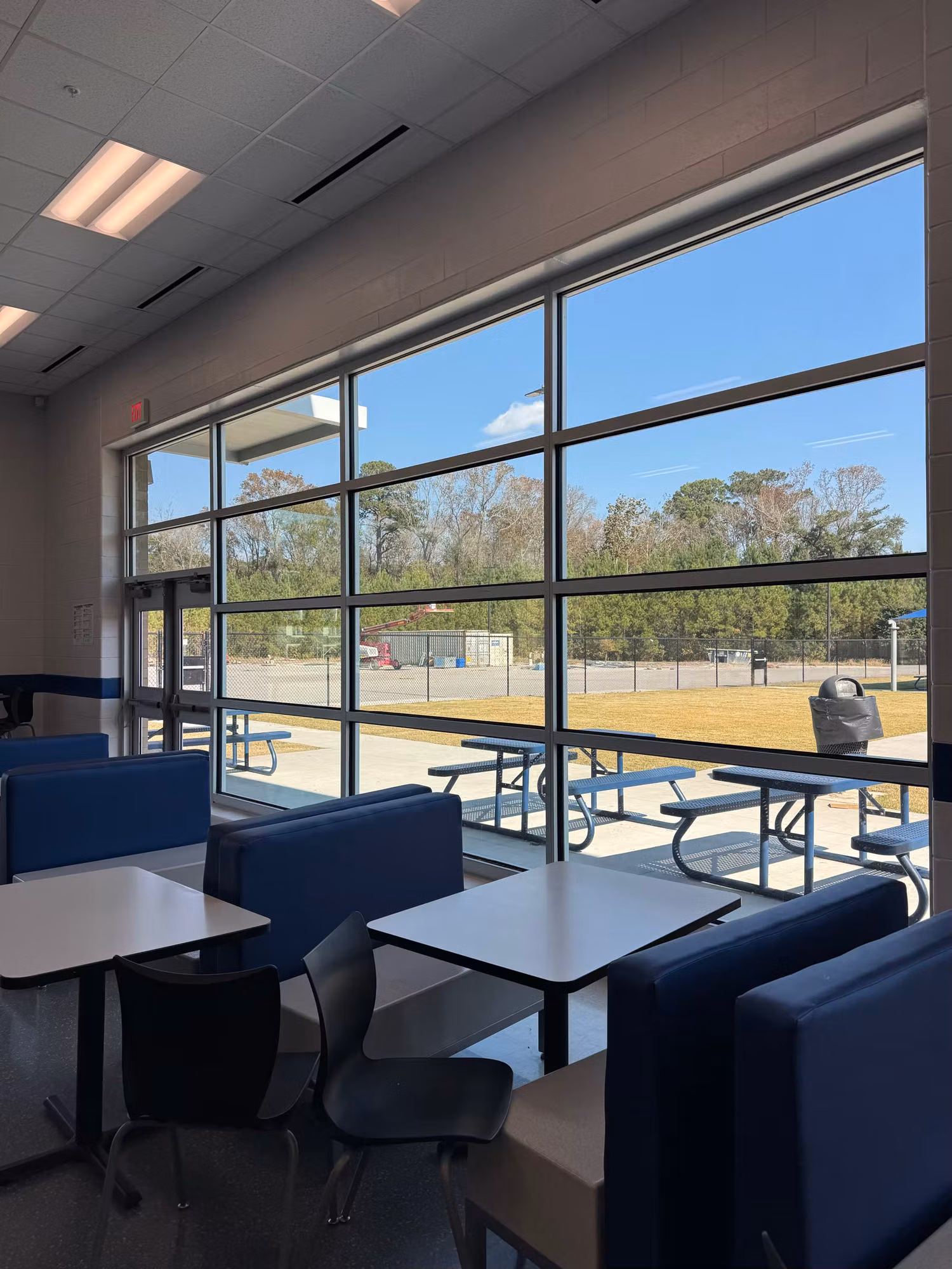 Cafeteria booth seating beside a tall tinted window wall looking out over a grass athletic field.