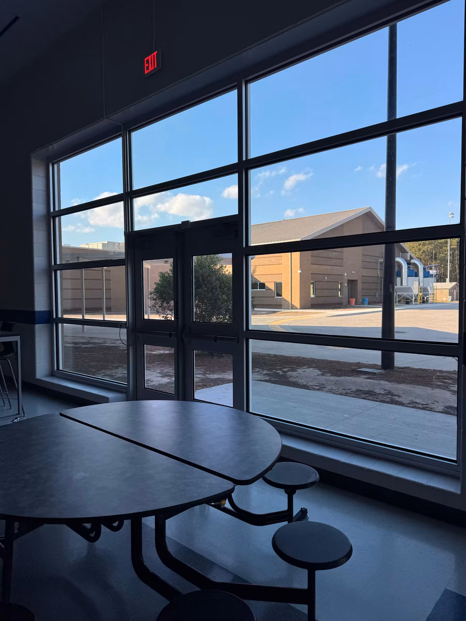 Cafeteria interior with a tinted floor-to-ceiling window wall cutting glare over the lunch tables.