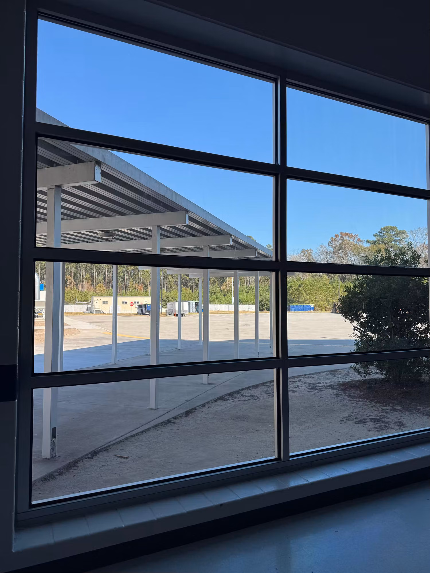 Tall mullioned commercial window with solar control film overlooking a covered walkway and parking lot.
