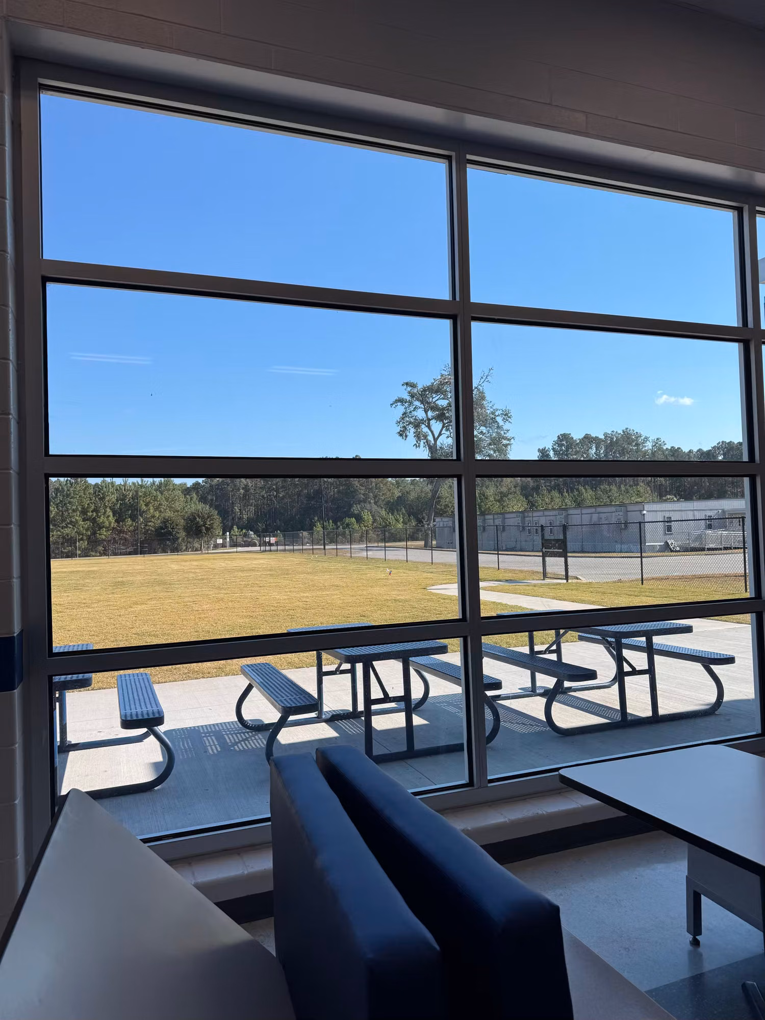 School commons window wall with solar control film overlooking picnic tables and an athletic field.