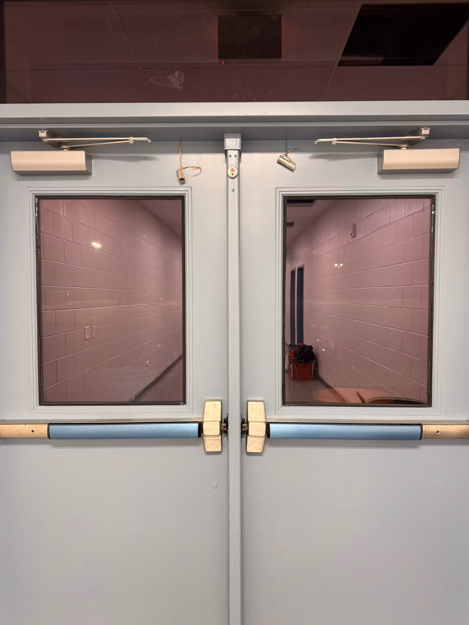Interior double doors with tinted vision panels opening onto a block-wall corridor.