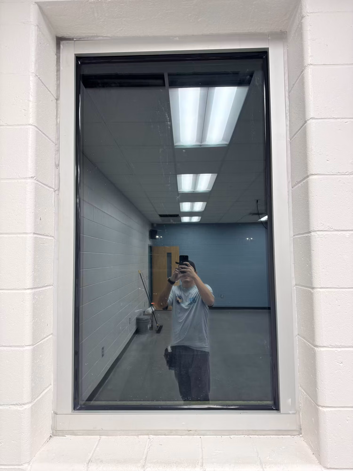 Tall fixed interior window with reflective tinted film mirroring the room's overhead lighting.