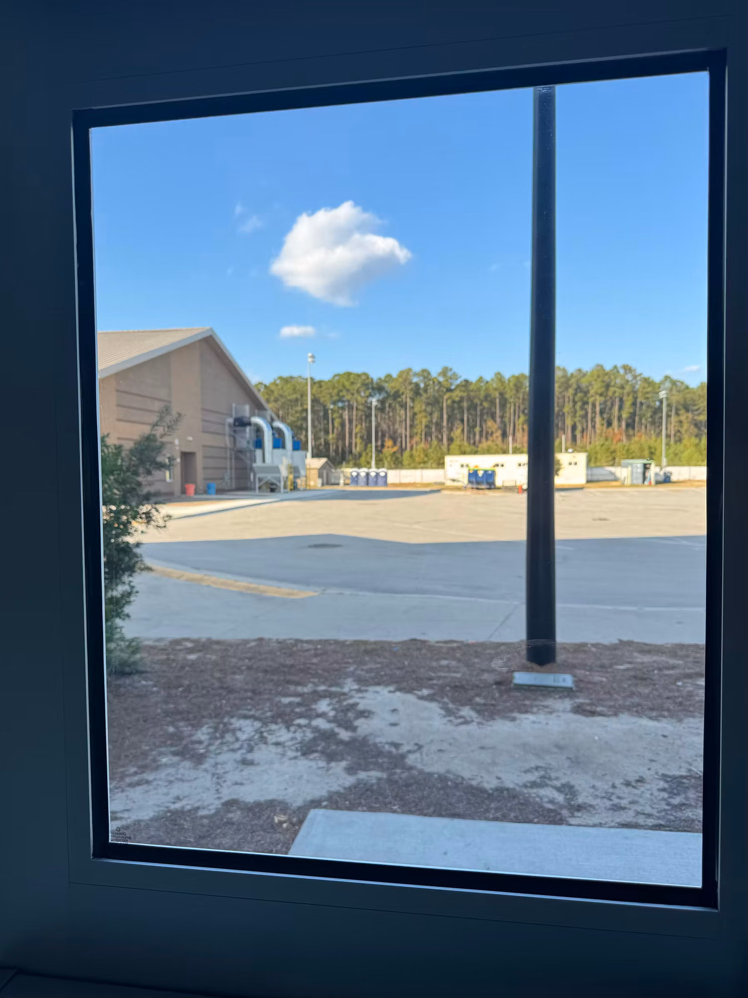 Large fixed window with darkened solar film framing a view of grounds, a building and trees.