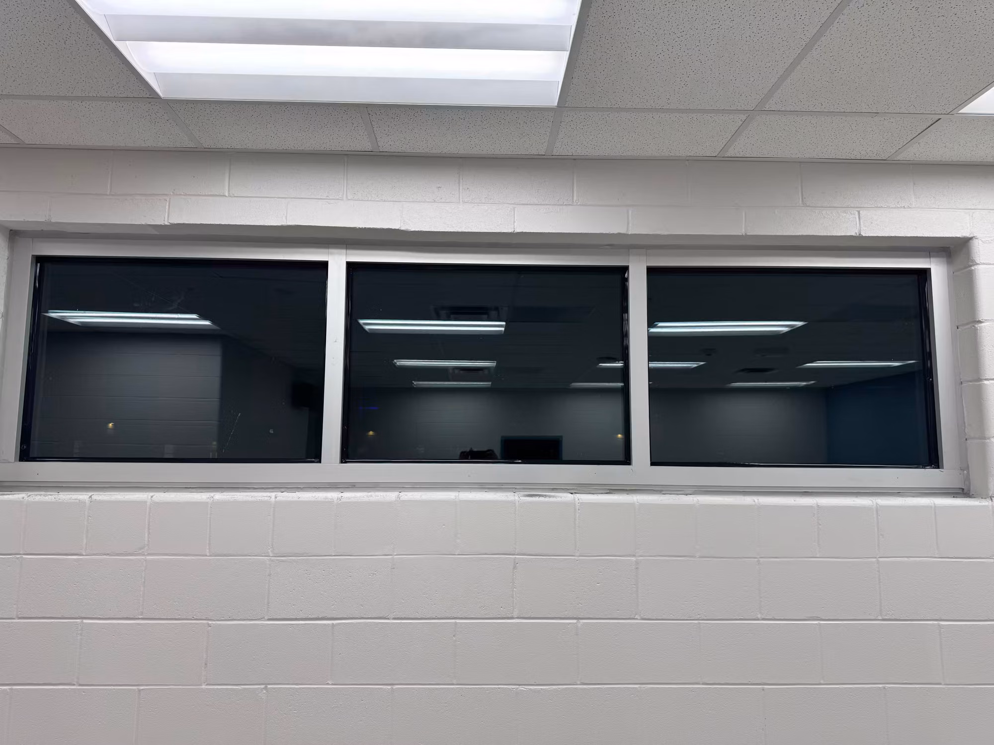 Horizontal band of three high interior windows in a white block wall darkened with reflective window film.