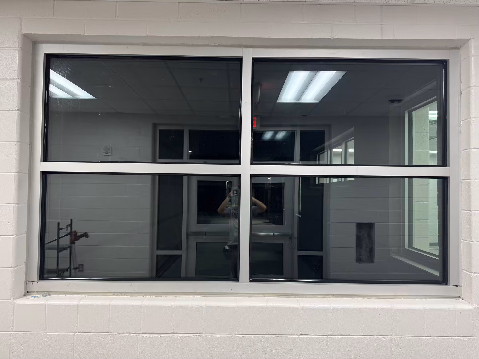Wide four-pane interior partition window with darkened film set into a painted block wall.