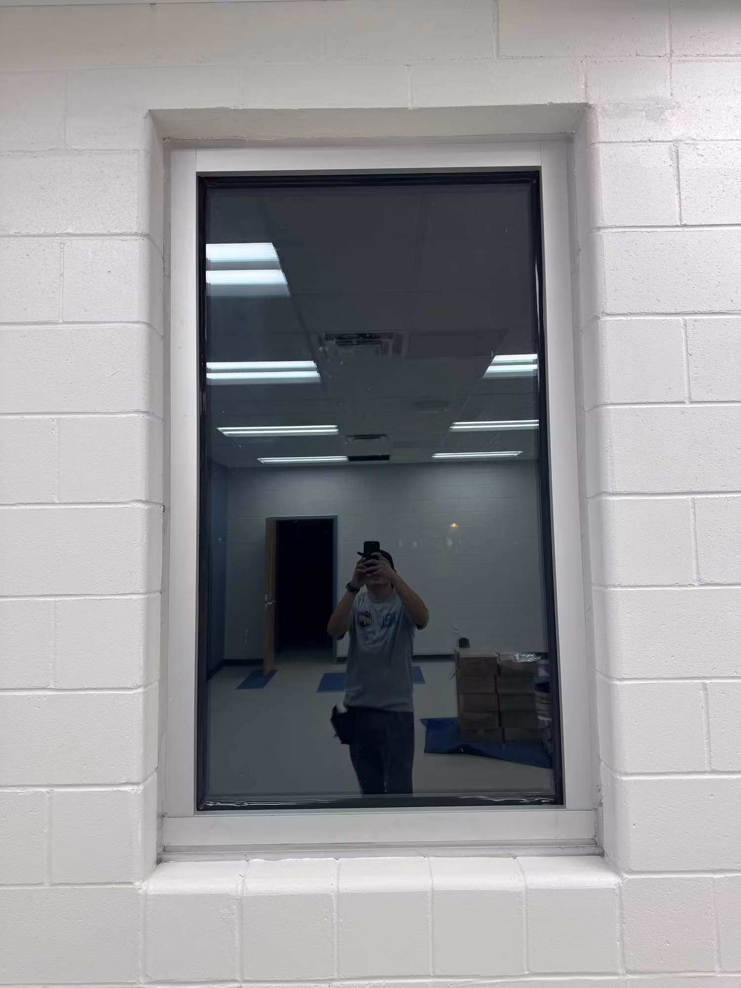 Interior block-wall window with dark reflective film overlooking an open room with stacked supplies.