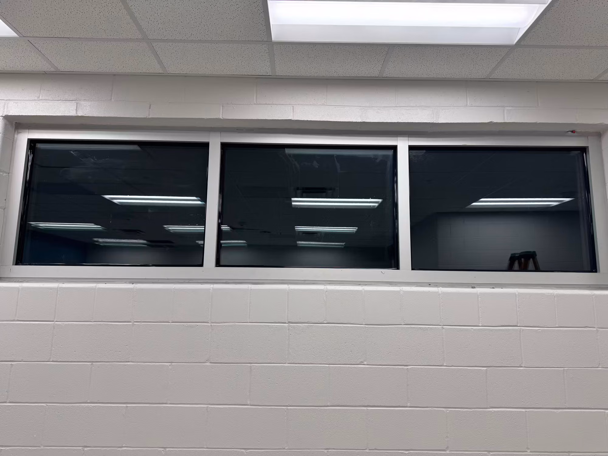 Row of three interior windows with dark reflective film set above a painted block knee wall.
