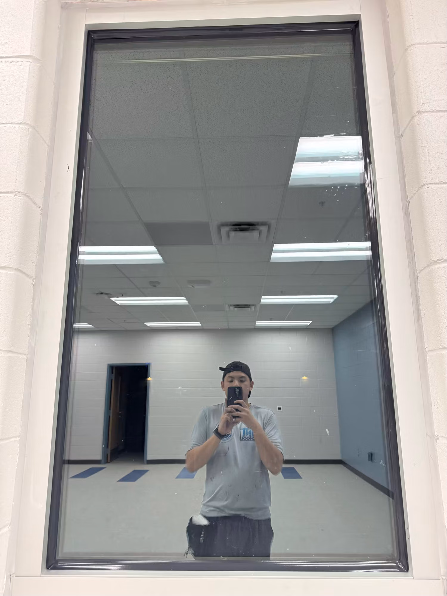 Tall interior window in a block wall covered with darkened reflective film mirroring the lit room beyond.