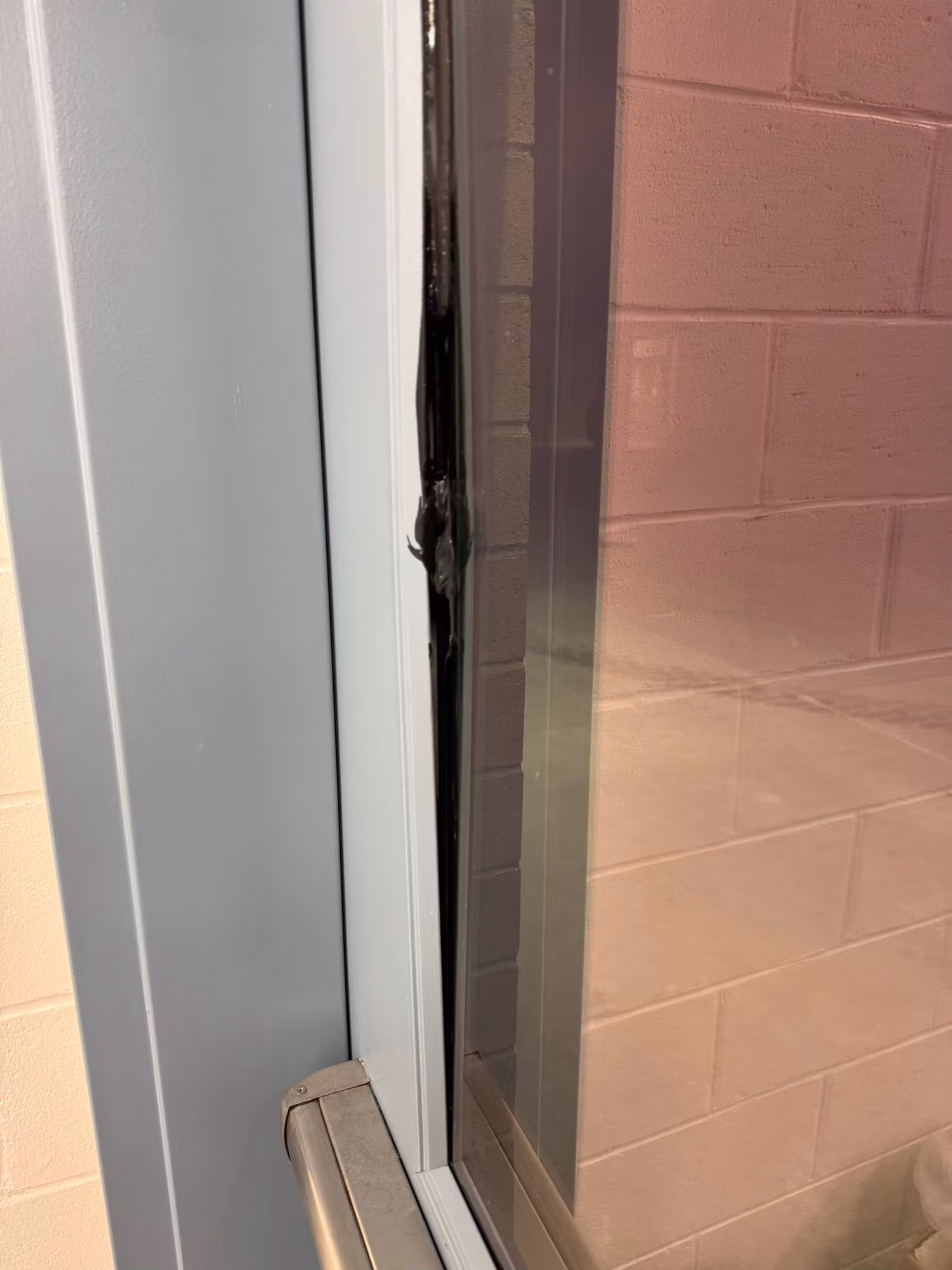 Close-up of a window edge where tinted film meets the frame and jamb against a block wall.