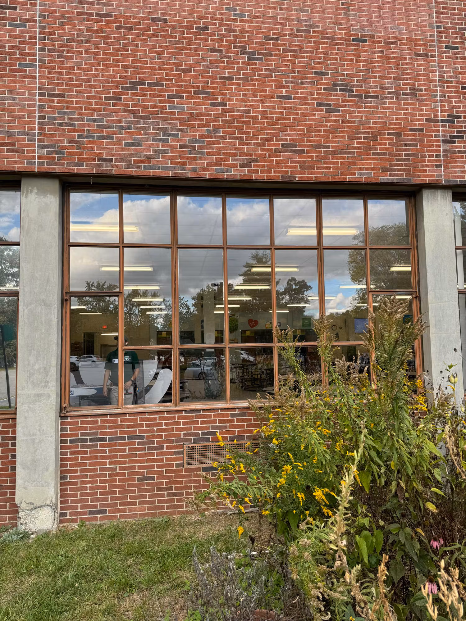 Exterior brick school wall with a large cafeteria window showing reflective solar control film and sky reflections.